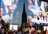 Crowd at a voting rally with large screen and church steeple in background